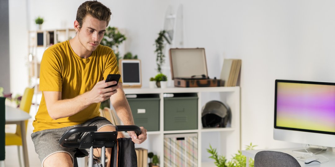 Man using mobile phone while cycling on exercise equipment at home