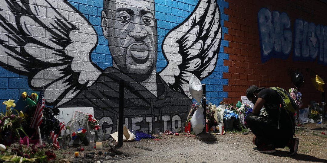 Man kneels in front of a memorial and mural that honors George Floyd at the Scott Food Mart corner store in Houston's Third Ward.