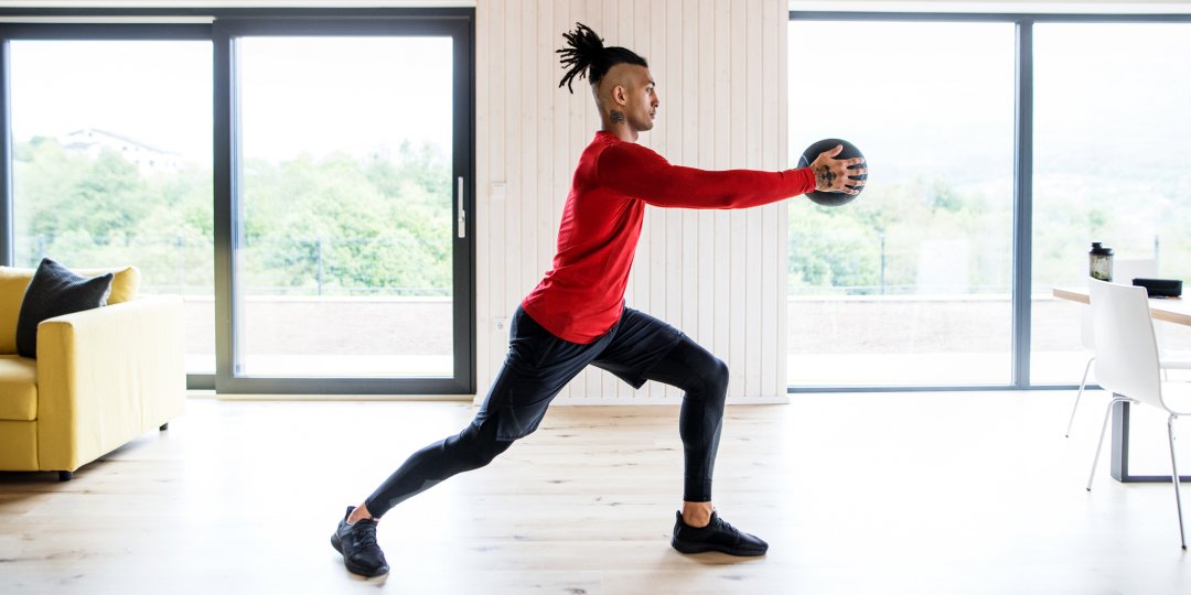 A side view of fit mixed race man with dreadlocks doing exercise with a ball at home