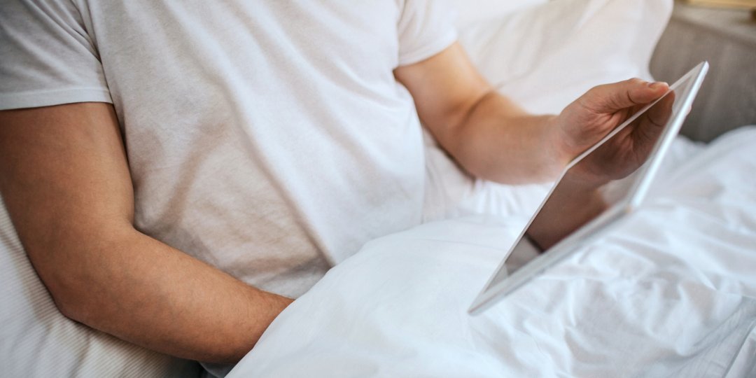 Guy sit in bed in the morning. He hold hand under blanket and masturbating