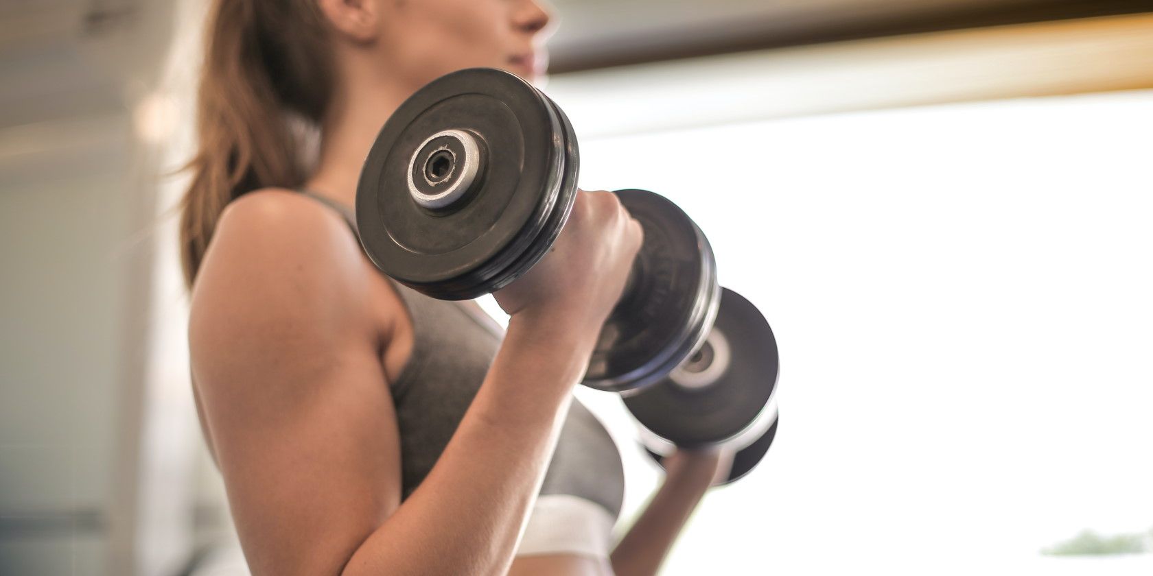 woman at the gym wearing grey sports top lifting black dumbbells