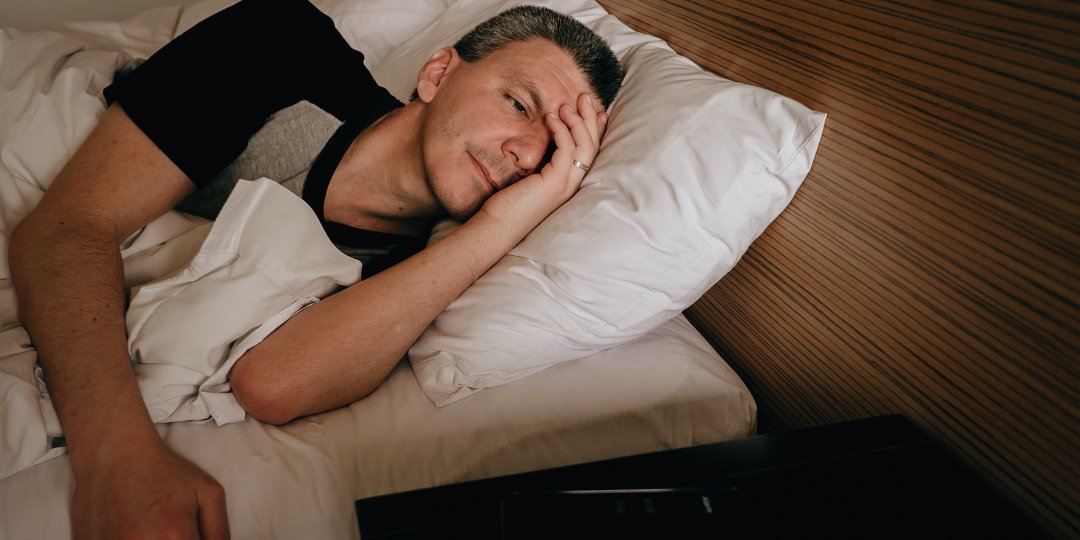 Adult man in bed looking at cell phone alarm